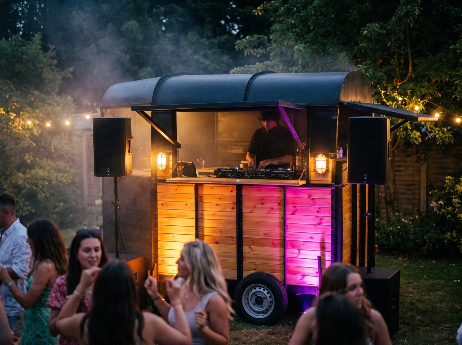 A DJ playing from inside The Box at night with speakers either side